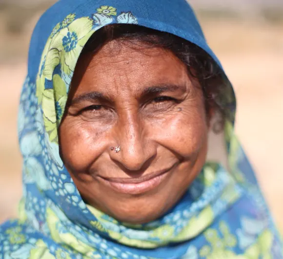 A smiling woman farmer wearing a blue patterned headscarf