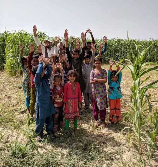 Children in a village field cheering with their arms raised